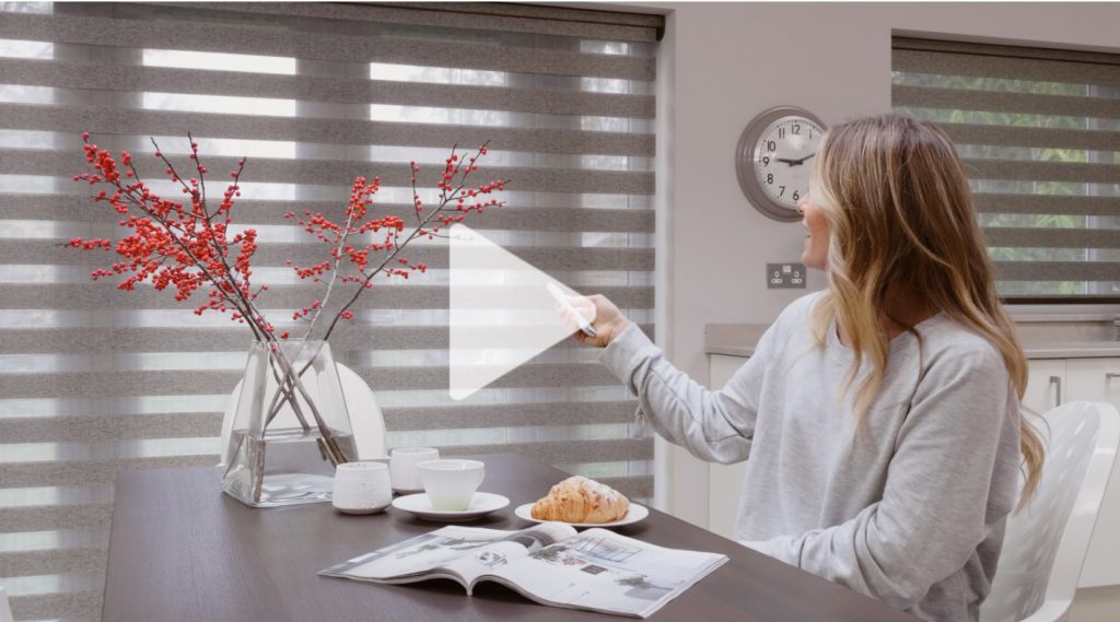 A woman using a remote control to manage electric Louvolite blinds in a kitchen