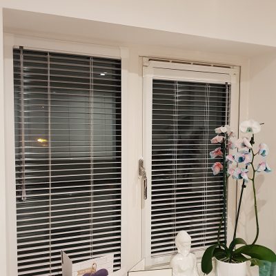 White perfect fit window blinds inside double glazed frame at night with potted orchid